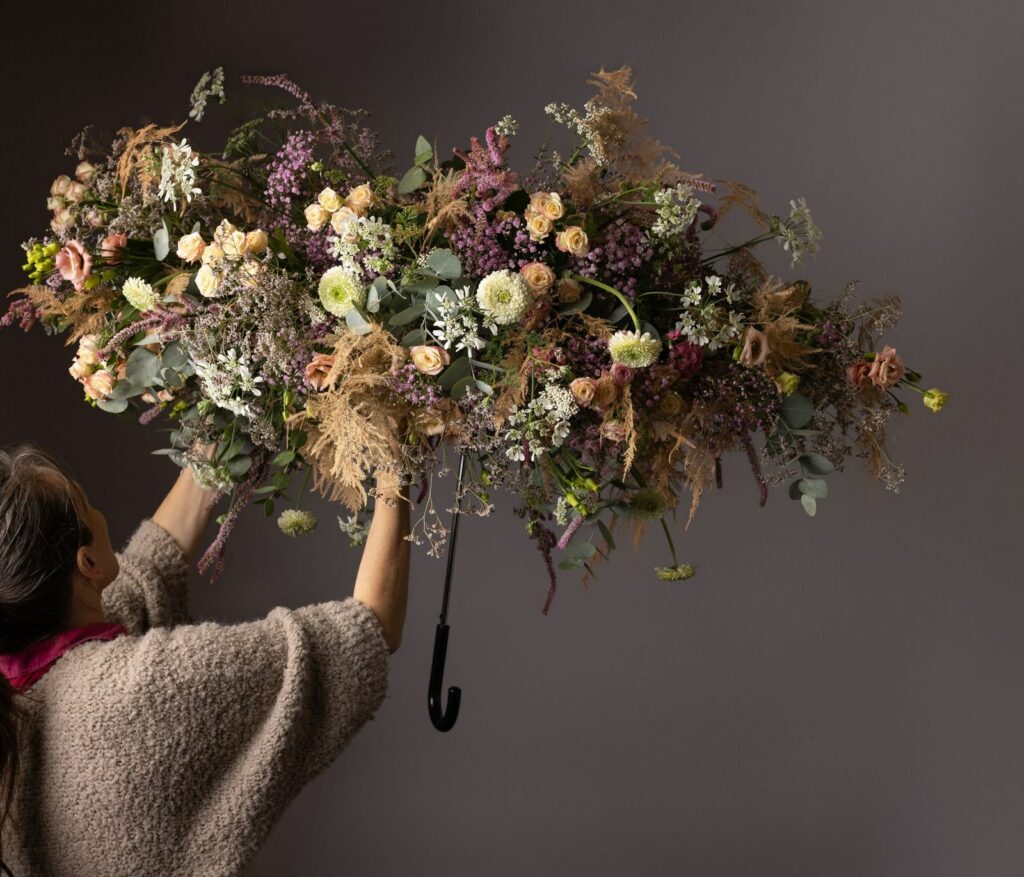 Laurence Requilé, vue de dos, ajuste à deux mains une installation florale suspendue au-dessus d'elle.