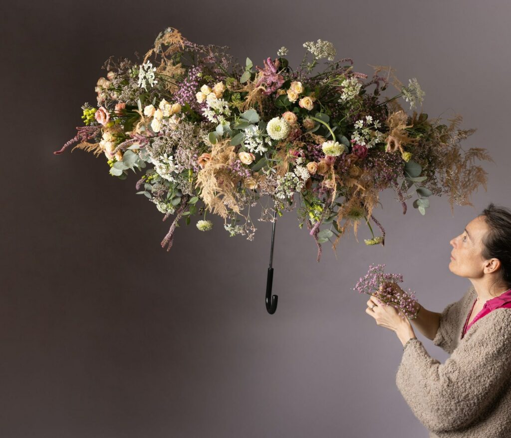Laurence Requilé tient une petite grappe de fleurs séchées devant une grande composition suspendue.