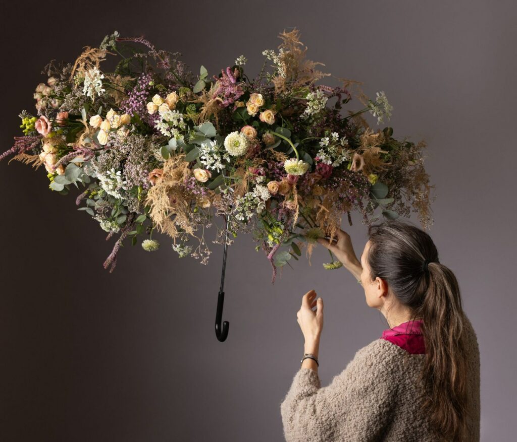 Laurence Requilé place une tige de fleurs séchées dans une composition suspendue, bras levé.