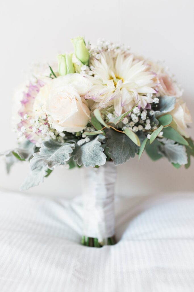 Bouquet de mariée en roses crème, dahlia blanc et gypsophile, rehaussé de feuillage gris, manche gainé de ruban.