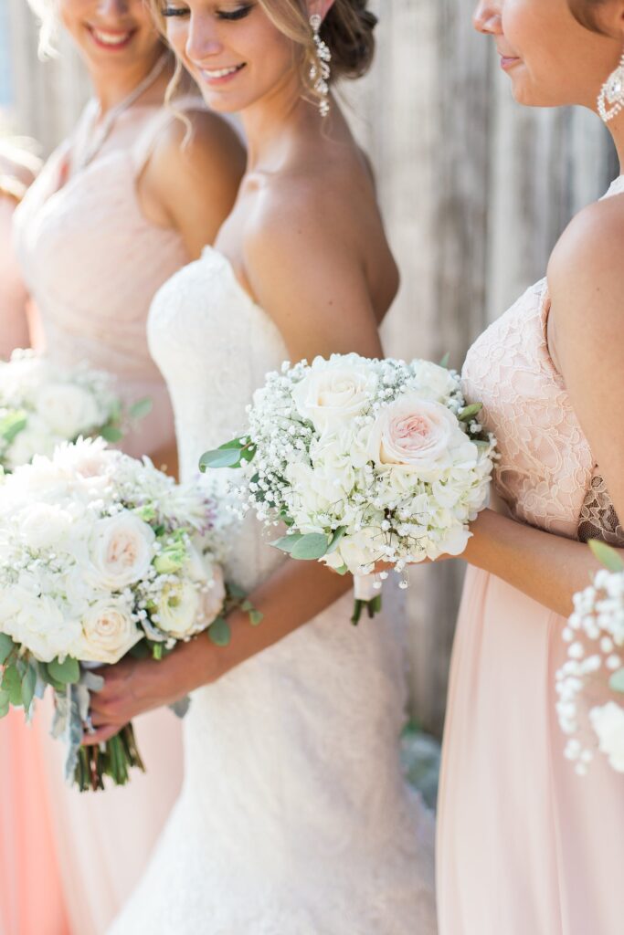 Une mariée et ses deux témoins en robes rose poudré, chacune tenant un bouquet blanc de roses, d'hortensia et de gypsophile.