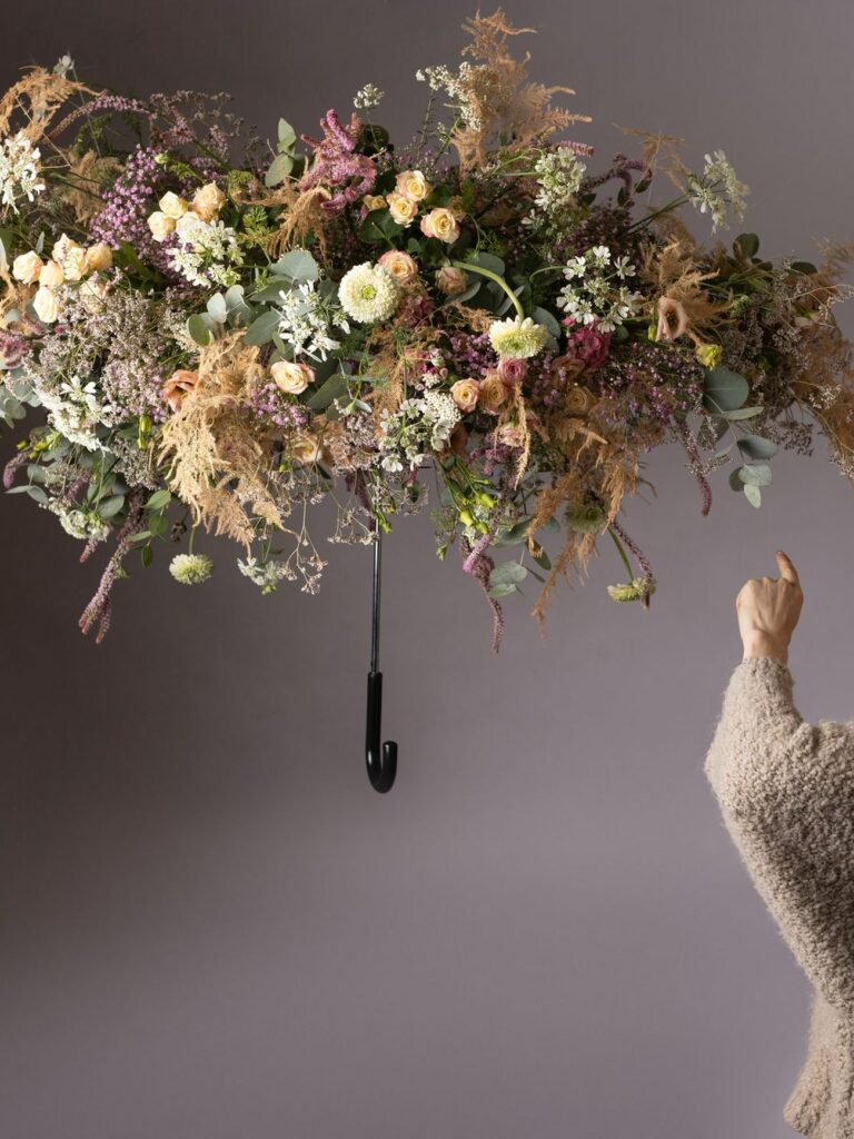 Composition aérienne de roses crème, d'eucalyptus et de graminées séchées, qu'une main vient effleurer.