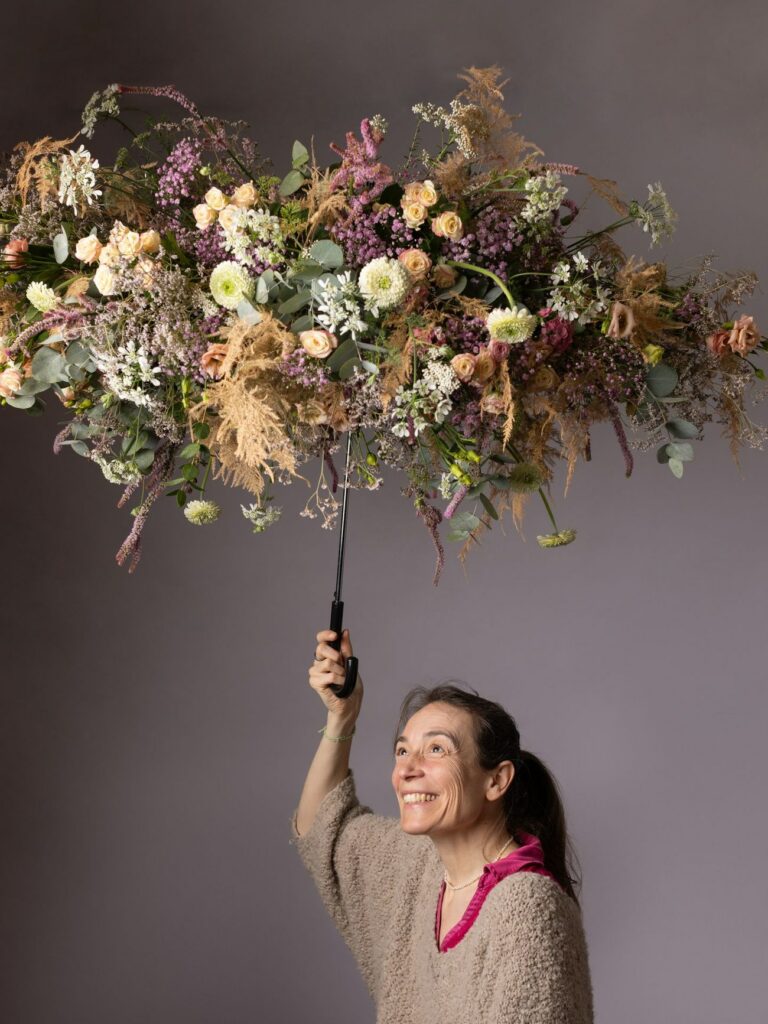 Laurence Requilé, souriante, tient à bout de bras le manche du parapluie fleuri au-dessus d'elle.